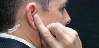 Man wearing an earpiece, touching his ear.