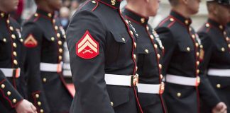 Marines in uniform standing in line, American flags displayed.