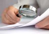 Person examining documents with a magnifying glass.