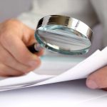 Person examining documents with a magnifying glass.