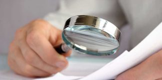 Person examining documents with a magnifying glass.