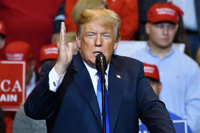 Man speaking at rally, red hats in background.