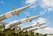 Multiple missiles pointed upward on launchers against blue sky.