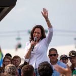 Woman speaking at outdoor event with raised hand.