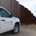 Border protection vehicle near a large metal fence.