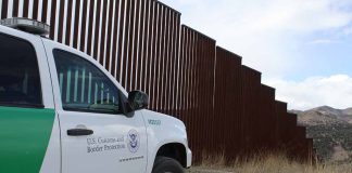 Border protection vehicle near a large metal fence.