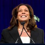 Woman smiling behind a podium with microphones.