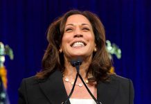 Woman smiling behind a podium with microphones.