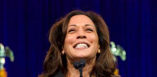 Woman smiling behind a podium with microphones.