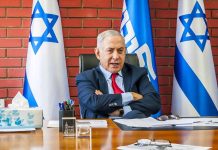 Man sitting at desk with Israeli flags behind.