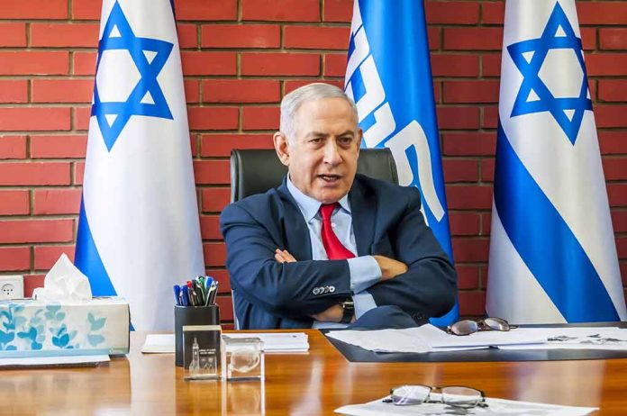 Man sitting at desk with Israeli flags behind.