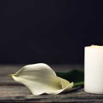 White candle and calla lily on wooden surface.