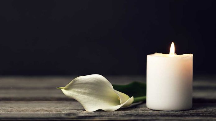 White candle and calla lily on wooden surface.