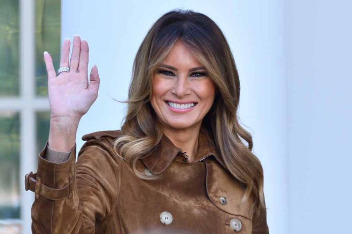 Woman smiling and waving in brown jacket.