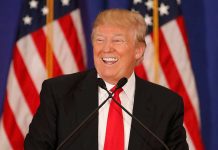 Smiling man speaking at podium with American flags.