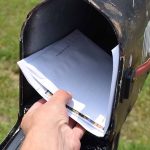 Hand placing mail in a black mailbox.