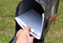 Hand placing mail in a black mailbox.