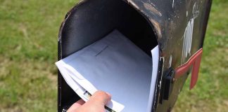 Hand placing mail in a black mailbox.