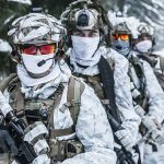 Soldiers in snow camo gear in snowy forest.