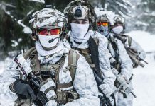 Soldiers in snow camo gear in snowy forest.