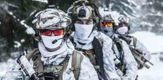 Soldiers in snow camo gear in snowy forest.