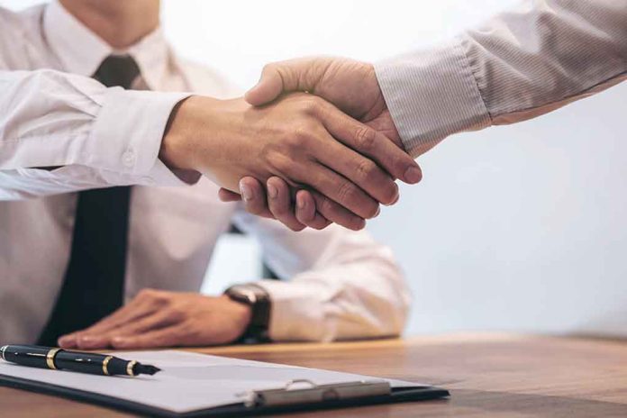 Two people shaking hands over a desk.