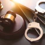 Gavel, books, and handcuffs on a table.