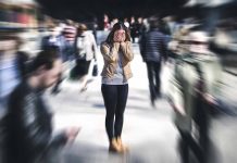 Person covering face amidst blurry crowd walking past.