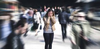 Person covering face amidst blurry crowd walking past.