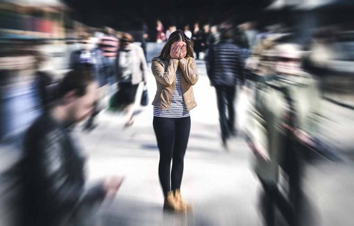 Person covering face amidst blurry crowd walking past.