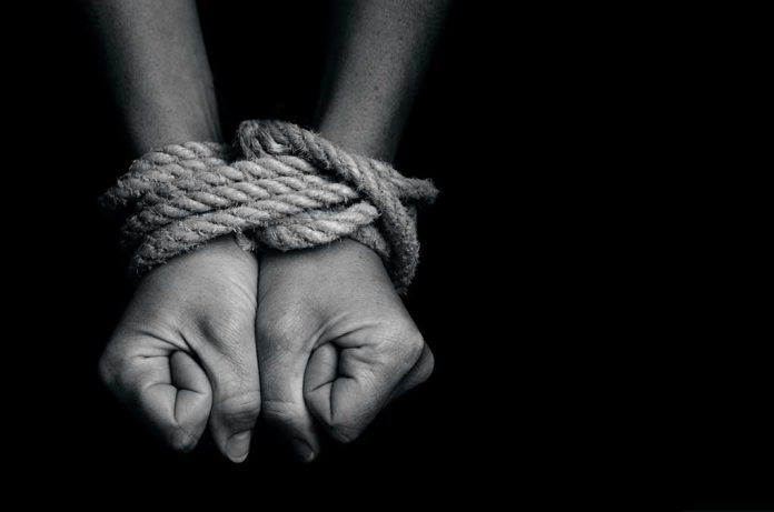 Hands bound with rope against a dark background.