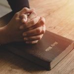 Hands praying on a Bible.