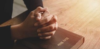 Hands praying on a Bible.