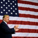 Man clapping in front of large American flag