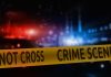 Crime scene tape with blurred police lights background.