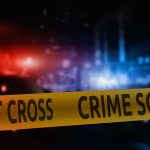 Crime scene tape with blurred police lights background.