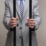 Person in handcuffs wearing suit behind bars