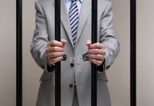 Person in handcuffs wearing suit behind bars