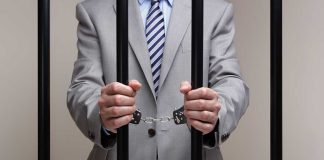 Person in handcuffs wearing suit behind bars