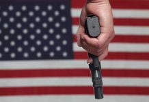 Hand holding gun against American flag backdrop.