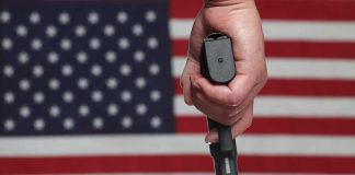 Hand holding gun against American flag backdrop.