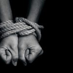 Hands bound with rope against a dark background.