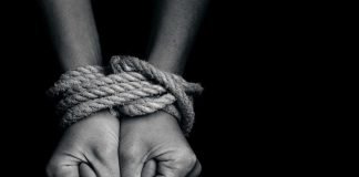 Hands bound with rope against a dark background.