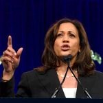 Woman speaking passionately at a podium, gesturing upward.