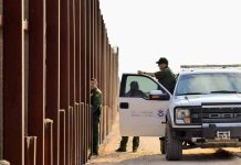 Border patrol agents near a tall metal fence.