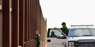 Border patrol agents near a tall metal fence.