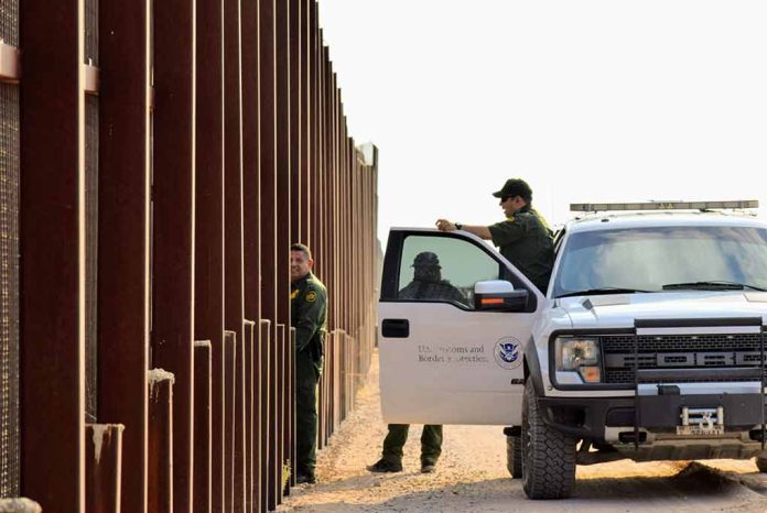 Border patrol agents near a tall metal fence.