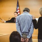 Man handcuffed in courtroom with supportive woman present