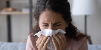 Woman sneezing into a tissue indoors.