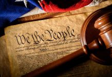 Gavel on U.S. Constitution with flag backdrop.